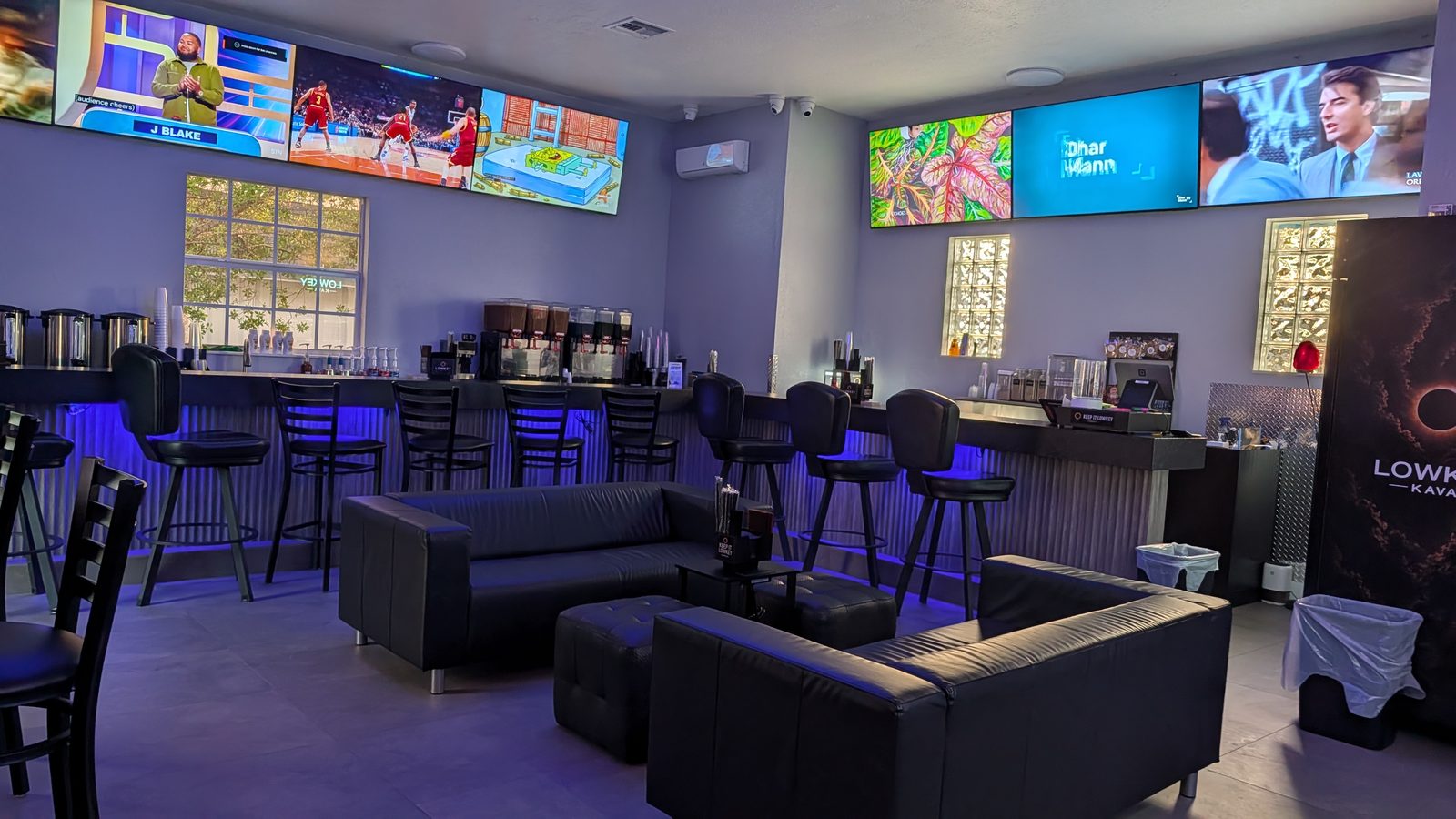 Wall of big-screen TVs showing sports above the bar and couches at Lowkey Kava West Palm Beach