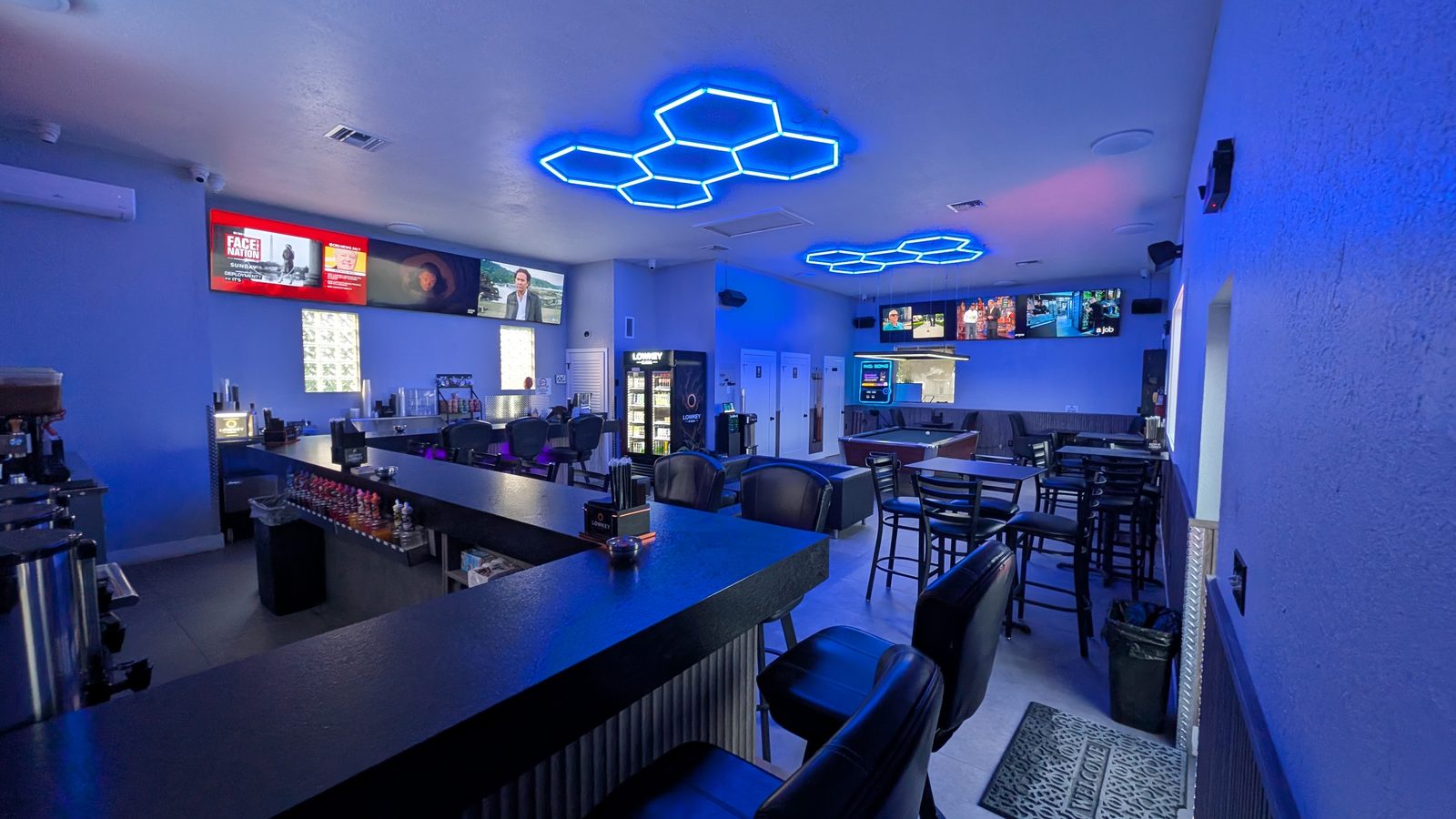 Inside the full bar at Lowkey Kava West Palm Beach with neon hex ceiling lights, big-screen TVs, and bar seating